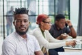 young African American man posing for the camera while sitting at a table in front of his colleagues Royalty Free Stock Photo