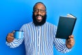 Young african american man reading book and drinking a cup of coffee smiling and laughing hard out loud because funny crazy joke Royalty Free Stock Photo