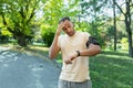 Young African American man runner, athlete in the park. A tired man counts his pulse on a fitness bracelet. Surprised
