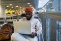 Young hipster black man sitting in airport terminal using laptop wear headphones and listening music Royalty Free Stock Photo