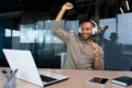 A young African American man sitting in office with laptop and headphones, listens to music, dances Royalty Free Stock Photo
