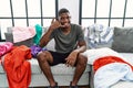 Young african american man sitting on the sofa with dirty laundry clothes smiling doing phone gesture with hand and fingers like Royalty Free Stock Photo