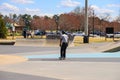 A young African American man on a skateboard in a skatepark surrounded by people sitting on benches with green umbrellas