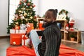 Young african american man smiling confident sitting by christmas tree at home Royalty Free Stock Photo