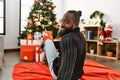 Young african american man smiling confident sitting by christmas tree at home Royalty Free Stock Photo