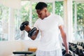 Young African American man standing and lifting a dumbbell with the rack at gym Royalty Free Stock Photo