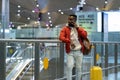 Young African American man traveler talking on mobile phone while standing with suitcase at airport Royalty Free Stock Photo