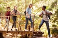 Young African American man turning to friends as they cross a footbridge during a hike in a forest, full length