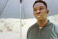 Young African American man under black umbrella in rain, sad. Fall or spring weather Royalty Free Stock Photo