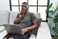 Young african american man using laptop at home sitting on the sofa laughing and embarrassed giggle covering mouth with hands, Royalty Free Stock Photo