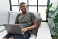 Young african american man using laptop at home sitting on the sofa looking away to side with smile on face, natural expression Royalty Free Stock Photo