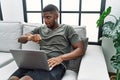 Young african american man using laptop at home sitting on the sofa looking at the watch time worried, afraid of getting late Royalty Free Stock Photo