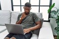Young african american man using laptop at home sitting on the sofa pointing to the eye watching you gesture, suspicious Royalty Free Stock Photo