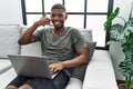 Young african american man using laptop at home sitting on the sofa smiling doing phone gesture with hand and fingers like talking Royalty Free Stock Photo