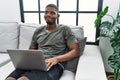 Young african american man using laptop at home sitting on the sofa smiling looking to the side and staring away thinking Royalty Free Stock Photo