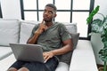 Young african american man using laptop at home sitting on the sofa thinking concentrated about doubt with finger on chin and Royalty Free Stock Photo