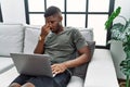 Young african american man using laptop at home sitting on the sofa tired rubbing nose and eyes feeling fatigue and headache Royalty Free Stock Photo