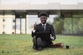 African-American man using laptop outdoors, sitting on the grass near office Royalty Free Stock Photo