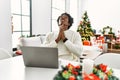 Young african american man using laptop sitting on the table by christmas tree begging and praying with hands together with hope Royalty Free Stock Photo