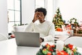 Young african american man using laptop sitting on the table by christmas tree doing ok gesture shocked with surprised face, eye Royalty Free Stock Photo