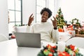 Young african american man using laptop sitting on the table by christmas tree shouting with crazy expression doing rock symbol Royalty Free Stock Photo