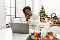 Young african american man using laptop sitting on the table by christmas tree sleeping tired dreaming and posing with hands