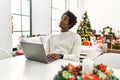 Young african american man using laptop sitting on the table by christmas tree smiling looking to the side and staring away Royalty Free Stock Photo