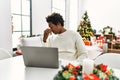 Young african american man using laptop sitting on the table by christmas tree tired rubbing nose and eyes feeling fatigue and Royalty Free Stock Photo