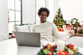 Young african american man using laptop sitting on the table by christmas tree winking looking at the camera with sexy expression, Royalty Free Stock Photo