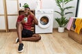 Young african american man using smartphone waiting for washing machine doing peace symbol with fingers over face, smiling Royalty Free Stock Photo