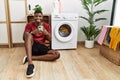 Young african american man using smartphone waiting for washing machine with a happy and cool smile on face Royalty Free Stock Photo