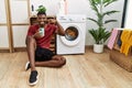 Young african american man using smartphone waiting for washing machine pointing with hand finger to face and nose, smiling Royalty Free Stock Photo