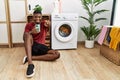 Young african american man using smartphone waiting for washing machine pointing to you and the camera with fingers, smiling Royalty Free Stock Photo