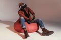 young african american man in virtual reality headset playing with joystick while sitting on bean bag chair Royalty Free Stock Photo