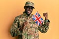 Young african american man wearing army uniform holding united kingdom flag pointing thumb up to the side smiling happy with open Royalty Free Stock Photo