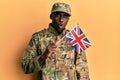 Young african american man wearing army uniform holding united kingdom flag scared and amazed with open mouth for surprise, Royalty Free Stock Photo