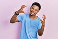 Young african american man wearing casual blue t shirt shouting frustrated with rage, hands trying to strangle, yelling mad Royalty Free Stock Photo