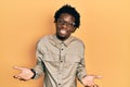 Young african american man wearing casual clothes and glasses clueless and confused expression with arms and hands raised Royalty Free Stock Photo