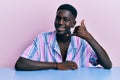 Young african american man wearing casual clothes sitting on the table smiling doing phone gesture with hand and fingers like Royalty Free Stock Photo