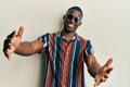 Young african american man wearing casual clothes and sunglasses looking at the camera smiling with open arms for hug Royalty Free Stock Photo