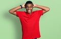 Young african american man wearing casual red t shirt relaxing and stretching, arms and hands behind head and neck smiling happy Royalty Free Stock Photo