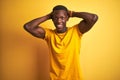 Young african american man wearing casual t-shirt standing over isolated yellow background Crazy and scared with hands on head, Royalty Free Stock Photo