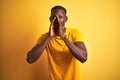Young african american man wearing casual t-shirt standing over isolated yellow background Shouting angry out loud with hands over Royalty Free Stock Photo