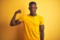 Young african american man wearing casual t-shirt standing over isolated yellow background Strong person showing arm muscle, Royalty Free Stock Photo