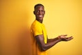 Young african american man wearing casual t-shirt standing over  yellow background pointing aside with hands open palms Royalty Free Stock Photo