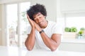 Young african american man wearing casual white t-shirt sitting at home sleeping tired dreaming and posing with hands together Royalty Free Stock Photo