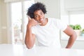 Young african american man wearing casual white t-shirt sitting at home smiling doing phone gesture with hand and fingers like Royalty Free Stock Photo