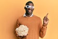 Young african american man wearing d glasses holding popcorns smiling happy pointing with hand and finger to the side Royalty Free Stock Photo