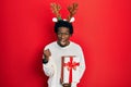 Young african american man wearing deer christmas hat holding gift angry and mad raising fist frustrated and furious while Royalty Free Stock Photo