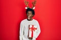 Young african american man wearing deer christmas hat holding gift angry and mad screaming frustrated and furious, shouting with Royalty Free Stock Photo